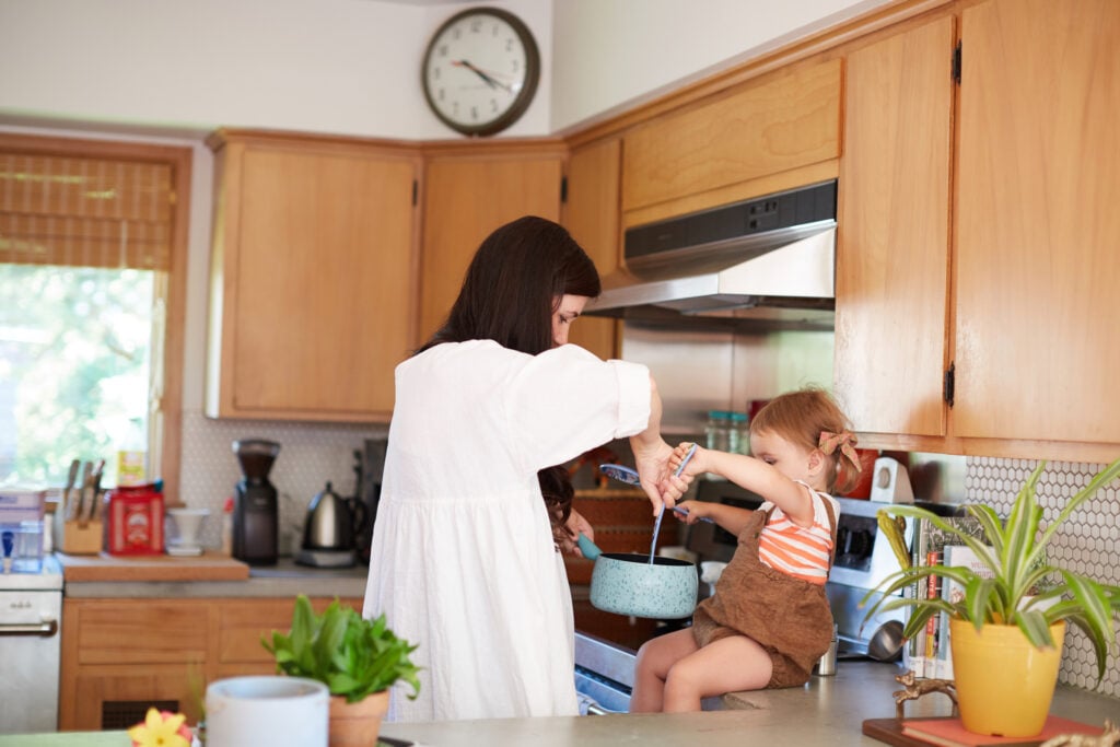 A Christian mom allowing her toddler daughter to help stir food in a pot, knowing her labor is not in vain
