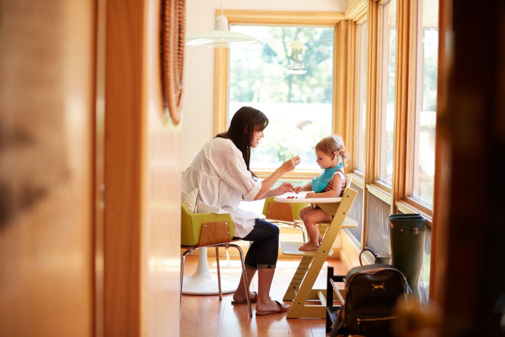A Christian mom feeding her toddler daughter, who sits in a high chair