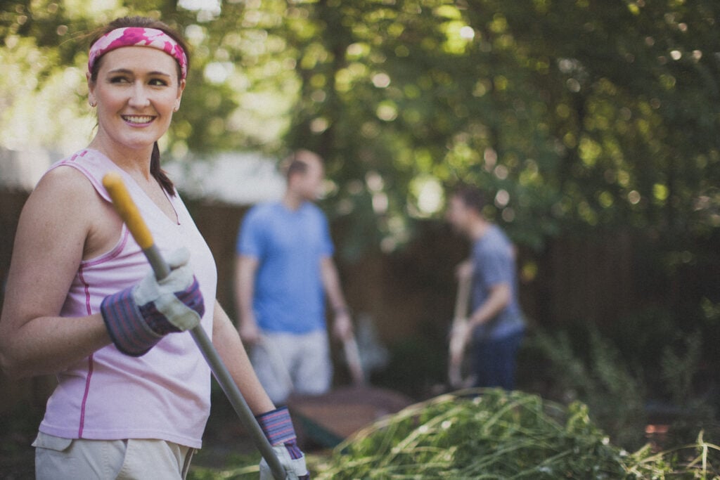 A Christian woman smiling as she does yardwork with work gloves on her hands