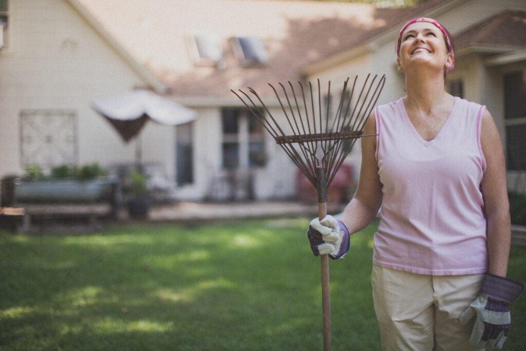 A Christian woman wearing work gloves looks up and smiles as she holds a rake
