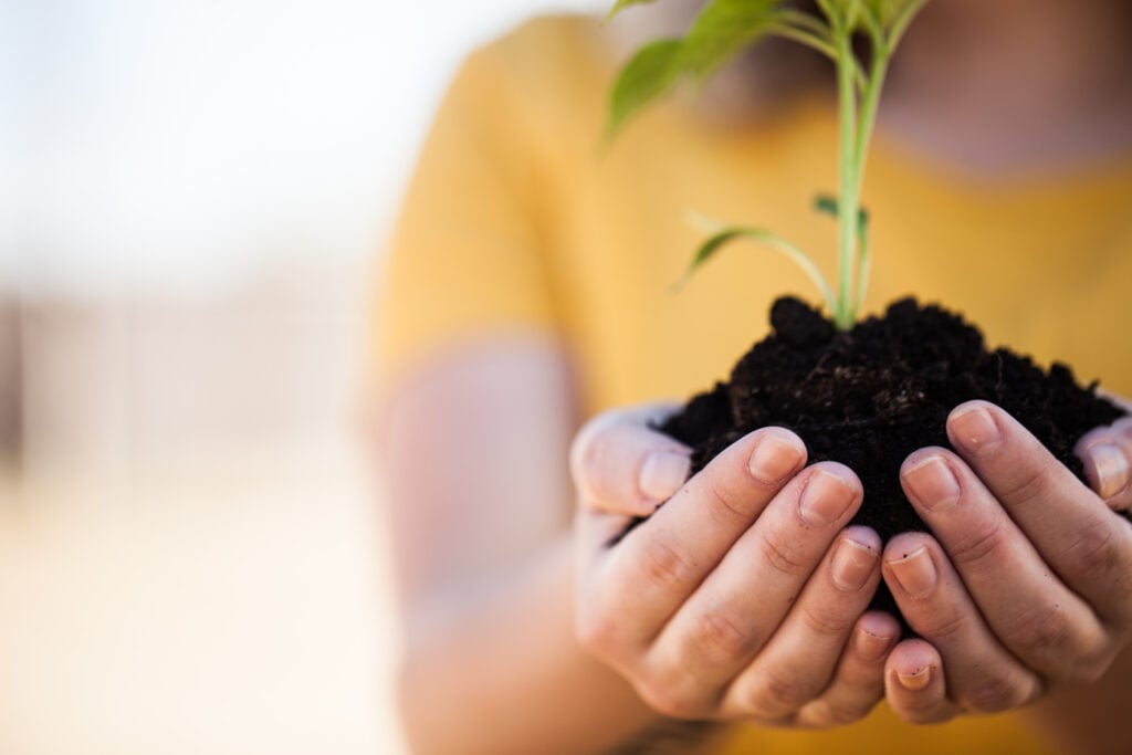 A Christian woman in a bright yellow t-shirt cupping a new plant in the palms of her hands