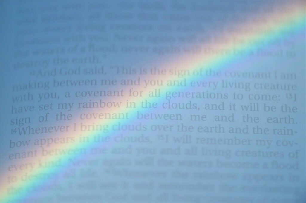 A rainbow overlaid on a page of the Bible—Genesis 9—where God establishes the rainbow as a sign of His covenant