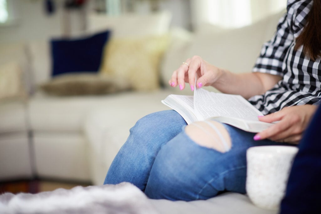 A Christian woman sitting on her living room couch paging through her Bible as she considers the impact of perfectionism in your quiet time