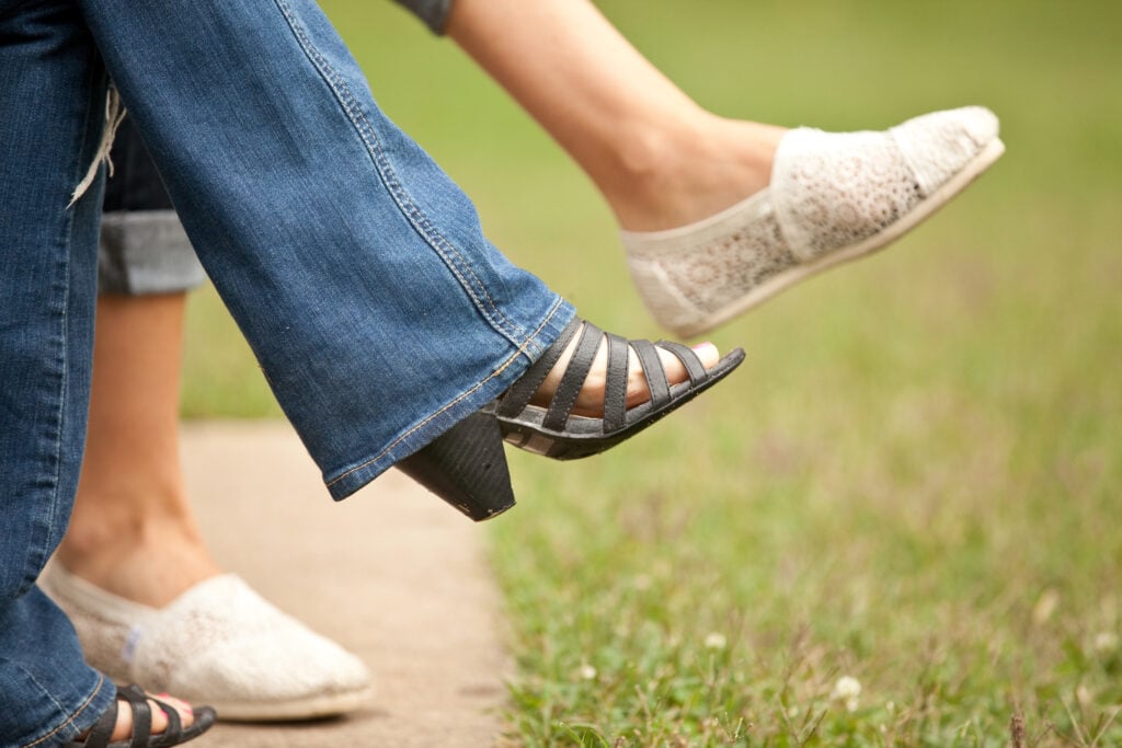 The feet of two Christian women who are sitting side-by-side on a park bench