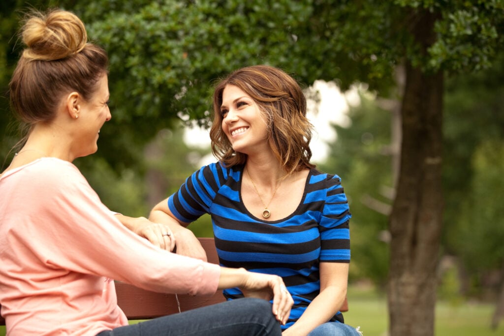 Two Christian women smiling at each other as they speak the truth in love while sitting on a park bench